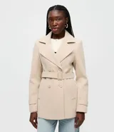 Saco Blue Steel de poliéster color beige, con cuello estructurado, solapas amplias, doble botonadura frontal, cinturón ajustable con hebilla, bolsillos laterales y trabillas en los puños.