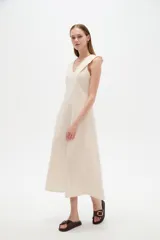 Vestido midi color beige claro, con cuello en V, sin mangas y corte entallado con pinzas.