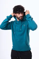 Buzo tipo canguro con capucha y cordones ajustables, confeccionado en felpa color beige. Presenta un pequeño logo bordado en el pecho y una etiqueta decorativa en el puño de la manga.