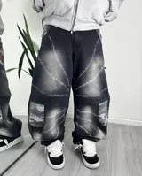 Jeans baggy negro de corte ancho con diseño degradado, estampado de líneas espinadas simulando púas y bolsillos laterales cargo con patrón de camuflaje en tonos grises.