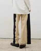 Pantalón de corte recto y tiro alto, confeccionado en algodón con diseño bicolor que combina paneles laterales en negro y panel central en beige, unidos por costuras visibles a contratono.