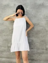 Vestido corto blanco con breteles finos que se atan en los hombros, corte recto y falda con volado en el ruedo.