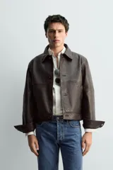Cazadora de corte cropped confeccionada en piel con acabado napado y costuras efecto vintage. Presenta cuello solapa, cierre frontal con botones, mangas largas con puños abotonados y bolsillos laterales de vivo.