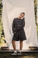 Buzo crewneck color chocolate, de tela rústica liviana, con estampado en el frente y la espalda. Presenta líneas blancas decorativas en el pecho y los brazos, y bordes deshilachados en los puños y el dobladillo.