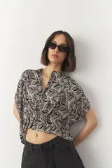Blusa corta de manga corta con estampado en blanco y negro, cuello mao y cierre frontal con botones. Cuenta con detalle de elástico fruncido en la cintura que genera un efecto peplum.