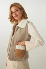 Chaleco corto de corte recto, confeccionado en lana fina sin teñir, con cuello de piel sintética y bolsillos frontales con detalles en cuero.