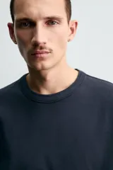 Camiseta de corte relajado confeccionada en tejido de algodón compacto. Presenta cuello redondo con acabado de rib doble y mangas cortas. Su apariencia única es resultado de un proceso especial de tintado y acabado.