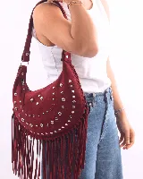 Bolso de hombro estilo boho confeccionado en gamuza color bordó. Presenta un diseño semicircular decorado con tachas metálicas plateadas dispuestas en líneas curvas y flecos largos en todo el borde inferior. Cuenta con cierre superior y correa ajustable para llevar al hombro.