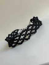 Gargantilla estilo choker tejida con pequeñas cuentas negras formando un diseño de red entrelazada, con cadena de ajuste metálica en la parte posterior.