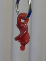 Aros colgantes compuestos por una argolla de acero quirúrgico y un dije de cristal de Murano en color rojo con forma de espiral retorcida.