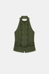Chaleco verde militar con cuello halter, espalda descubierta y cierre frontal con cremallera oculta. Presenta detalles de falsos botones dorados y ribetes en contraste, con trabillas en los laterales.