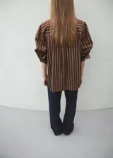 Camisa de algodón con diseño de rayas verticales en tonos marrón y beige, de manga larga, cuello camisero y cierre frontal de botones.