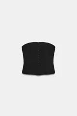 Top tipo corset de escote recto y hombros descubiertos, con cierre frontal mediante ganchos metálicos y costuras verticales estructuradas.