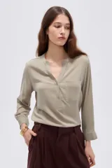 Blusa de viscosa color beige con cuello en V, cierre parcial de botones frontales, bolsillo en el pecho y mangas 3/4.