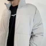 Campera puffer color gris claro, con cuello alto y cierre frontal con cremallera.