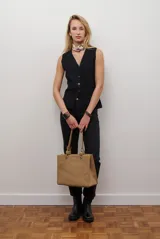 Chaleco tejido de punto en color beige, con escote en V, cierre frontal con botones oscuros y bolsillos frontales decorativos.