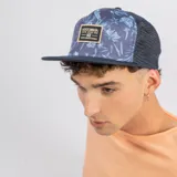 Gorro tipo trucker con frente estampado floral en tonos azules y paneles traseros de malla en color azul oscuro. Presenta un parche rectangular con el logo de la marca en el frente y visera plana.