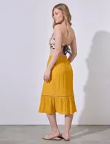 Falda midi color mostaza, de gasa bambula con pretina smock, lazo de ajuste, volado en el ruedo y aplique de puntilla.