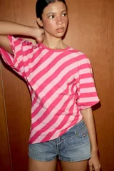 Top de algodón con estampado de rayas diagonales en tonos fucsia y rosado. Presenta cuello redondo, mangas cortas tipo murciélago y un diseño de bajo asimétrico.