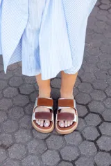 Sandalias bajas con base color suela, tiras anchas horizontales de cuero color marrón y plateado.