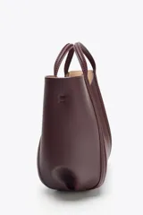 Bolso de mano tipo mini city, color borgoña, con pespuntes en contraste. Presenta asa de mano y asa bandolera extraíble. Incluye una bolsa interior extraíble con cierre de cremallera.