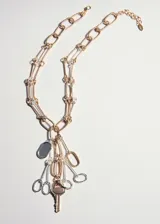Collar de diseño metálico con cadenas combinadas en tonos dorados y plateados, con múltiples dijes colgantes que incluyen una llave y eslabones decorativos.