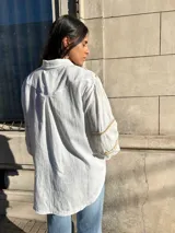 Camisa blanca de mangas largas con detalles de puntilla beige en cuello y puños, y cierre frontal con botones.