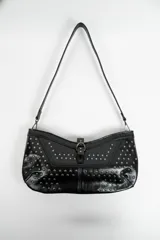 Cartera negra de hombro con diseño de tachas metálicas en la solapa y el cuerpo. Tiene una correa ajustable y un cierre de hebilla decorativo en el frente.