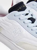 Zapatillas urbanas de corte bajo con exterior de ante blanco, detalles en gris y azul celeste, y refuerzo en el talón de cuero burdeos. Presentan el logo de la marca bordado en el lateral y en la parte trasera.