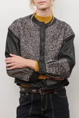 Chaqueta bomber color bordó con mangas de cuero sintético marrón y cuerpo de tweed con patrón de espiga. Cierre frontal con botones a presión y cuello redondo.