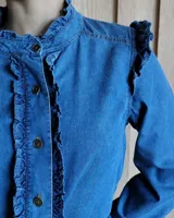 Camisa de denim azul con volados en el frente, cuello y hombros, de manga larga y corte clásico. Confeccionada en algodón.