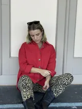 Camisa roja de corte holgado, con cuello clásico, cierre frontal con botones, mangas largas con puños abotonados, dos bolsillos con solapa en el pecho y ruedo recto.