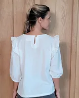 Blusa blanca de algodón tussor, con cuello redondo, mangas 3/4 abullonadas y detalle de volados en los hombros.