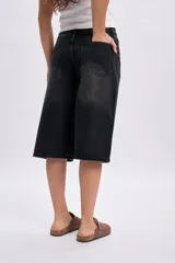 Bermuda de jean negro con efecto acid wash y diseño amplio de corte bermuda, con bolsillos laterales y traseros, y cierre frontal con botón y cremallera.