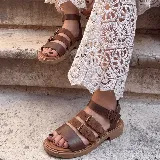 Sandalias marrones de diseño plano con plataforma baja, múltiples tiras frontales con hebillas metálicas ajustables y tira en el tobillo.