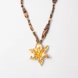 Collar con dije de flor grande en tono dorado brillante, suspendido de una cinta de tela con estampado animal print y detalles de cuentas doradas.