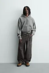 Pantalón de corte relaxed fit confeccionado en algodón, color gris oscuro. Presenta bolsillos delanteros, bolsillos laterales tipo cargo en las perneras y cierre frontal con cremallera y botón.
