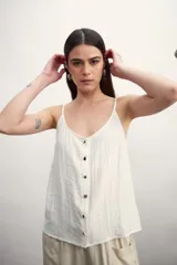 Musculosa color blanco roto con escote en V y botones frontales. La tela presenta una textura arrugada o plisada.