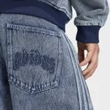 Jeans de mezclilla Adidas de pierna recta, efecto acid wash, con corte holgado, tiro medio y las clásicas tres tiras laterales. Cuenta con bordado del trébol de la marca.