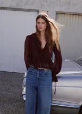 Blusa fluida color bordó, con escote en V, mangas largas con volantes en los puños y detalles de volantes en el frente y el cuello.