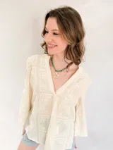 Blusa blanca de broderie con cuello mao y escote en V, mangas largas acampanadas y bordados calados.