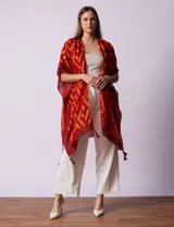 Kimono ligero de poliéster con estampado geométrico en tonos rojo oscuro y naranja. Presenta mangas anchas y terminación con borlas en los ruedos.