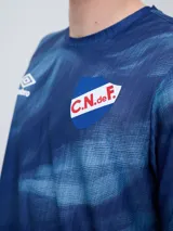 Remera de entrenamiento Umbro del Club Nacional de Football, modelo Press, para hombre. Diseño en tonos de rojo con patrón estampado tipo humo o abstracto, cuello redondo y mangas cortas. Incluye el logo de Umbro y el escudo del club en el pecho.