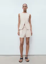 Short de tiro alto en color beige, con diseño recto, detalle de pinzas delanteras y bolsillos laterales. Cuenta con cierre oculto de botón, gancho y cremallera.