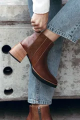 Bota corta de cuero color marrón, con diseño de texturas combinadas en los laterales y elástico. Presenta un taco medio de madera y suela de goma negra.