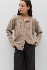 Saco de punto color rosa, con cuello redondo, cierre frontal con botones forrados en crochet y mangas largas. Presenta un delicado bordado floral artesanal que cae desde los hombros y detalles de calados en los puños y el ruedo.