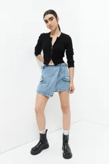 Minifalda de jean celeste con corte asimétrico, bolsillos de parche con solapa y tiras ajustables con hebillas en los laterales.