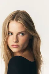 Top negro de manga larga, tejido en punto acanalado, con escote amplio tipo barco que deja los hombros al descubierto y un leve escote en V. El bajo y los puños terminan con un ribete fino de volados.