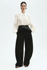 Blusa oversized de tejido transparente color crudo, con detalles bordados en relieve, cuello camisero, cierre frontal de botones y mangas largas abullonadas con puños ajustados.