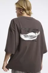 Remera de corte boxy color gris oscuro, con cuello redondo y mangas cortas. Presenta un diseño estampado localizado en la parte superior del pecho.